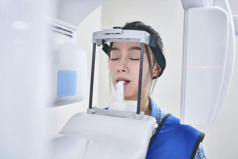 Patient undergoing Cone Beam Computed Tomography (CBCT) dental scan, head positioned with bite block and laser alignment guides.